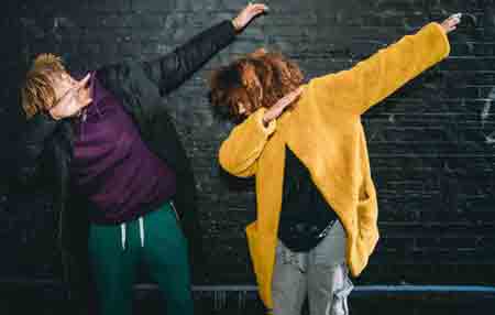 Two young adults making dabbing movement against a black bricks wall. They are wearing hip and colorful clothes.
